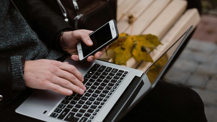 ছবিতে একজন লোক ল্যাপটপ এবং ফোন ব্যবহার করছে