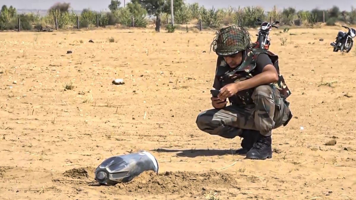 A security personnel inspects the debris of an unidentified projectile which landed amid the military