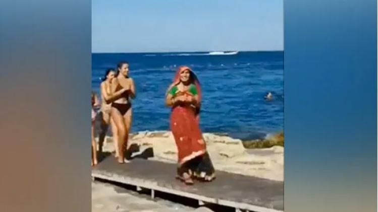 In the clip, a woman is wearing a saree while strolling on a beach.