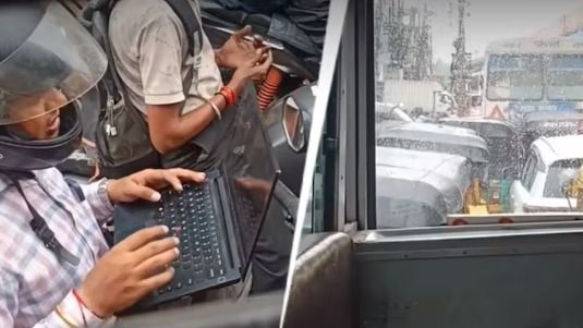 ट्रैफिक जाम में बाइक पर बैठ कर काम करते हुए युवक की तस्वीर 
