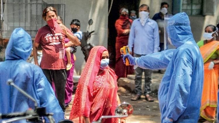 मुंबई के धारावी में सुरक्षात्मक सूट पहनकर लोगों की जांच करता एक डॉक्टर