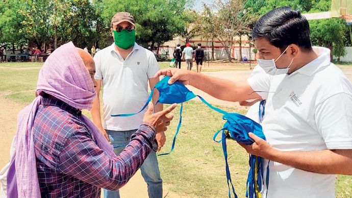 सुरक्षा पहले रिलायंस फाउंडेशन के कर्मी फेस मास्क बांटते हुए