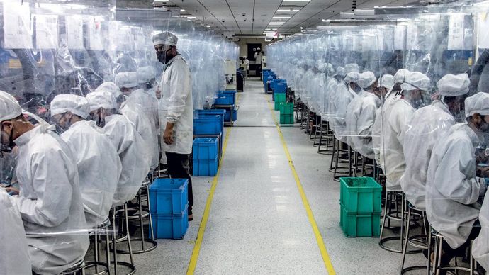 नया तौर-तरीका उत्तर प्रदेश के नोएडा में लावा फोन फैक्टरी में प्लास्टिक के परदे में मास्क के साथ कर्मचारी
