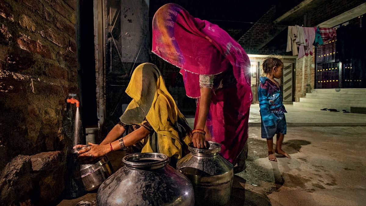 हंसी-खुशी की धारा राजस्थान के सिंद्रठ गांव में रात में अपने घर के सुकून में नल से पानी भरतीं महिलाएं