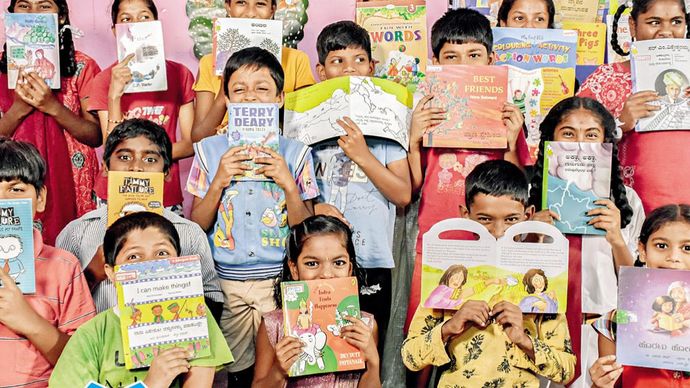 उत्साही पाठक बेंगलूरू की बुगुरी लाइब्रेरी में कहानी की किताबों के पीछे प्रफुल्लित बच्चे