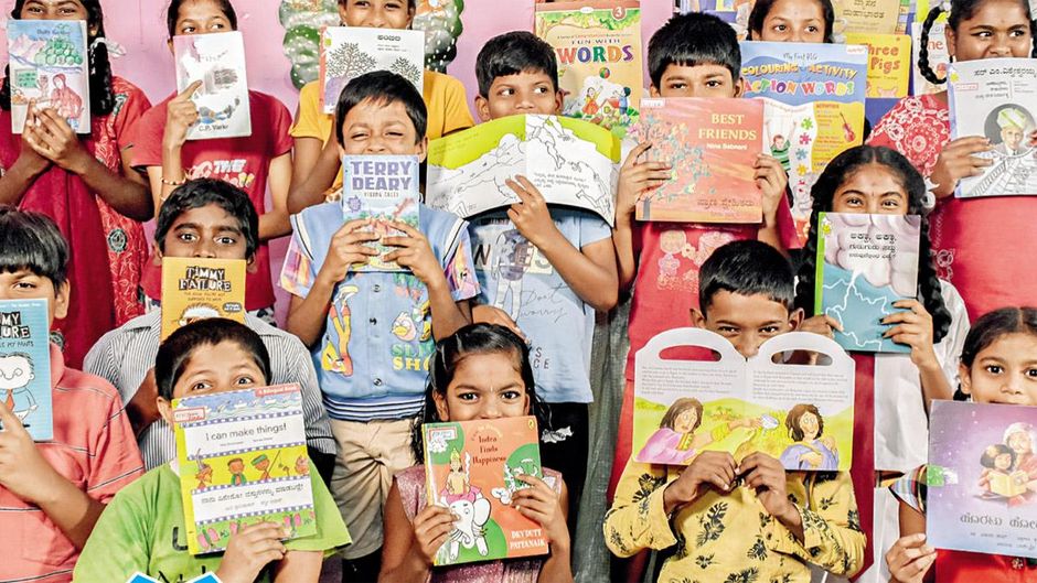 उत्साही पाठक बेंगलूरू की बुगुरी लाइब्रेरी में कहानी की किताबों के पीछे प्रफुल्लित बच्चे